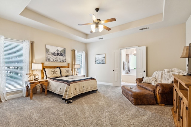 bedroom with ceiling fan, ensuite bathroom, a tray ceiling, and carpet floors