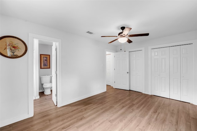 unfurnished bedroom featuring light wood-type flooring, ceiling fan, ensuite bathroom, and multiple closets