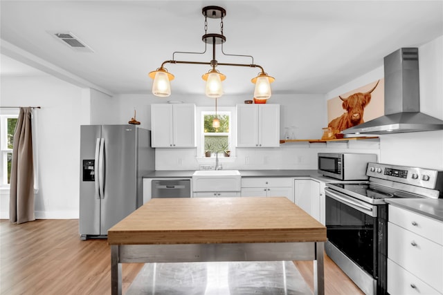 kitchen with wall chimney exhaust hood, a wealth of natural light, stainless steel appliances, and white cabinets