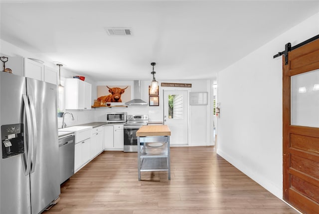 kitchen with a barn door, stainless steel appliances, white cabinetry, wall chimney range hood, and wooden counters