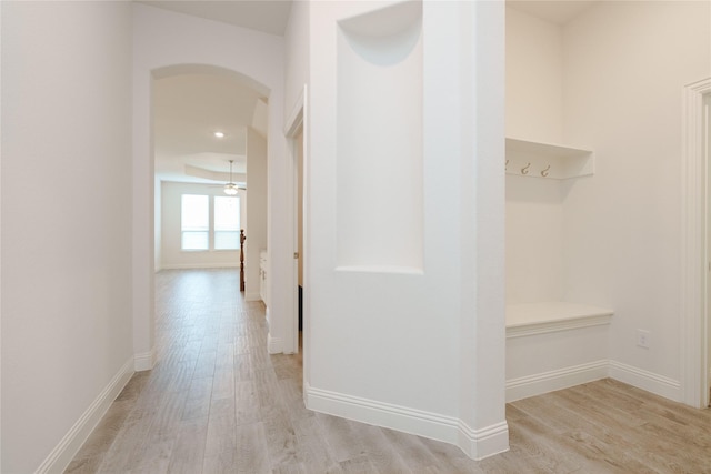 hall with light wood-style flooring, baseboards, and arched walkways