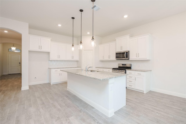 kitchen with visible vents, an island with sink, white cabinetry, arched walkways, and appliances with stainless steel finishes