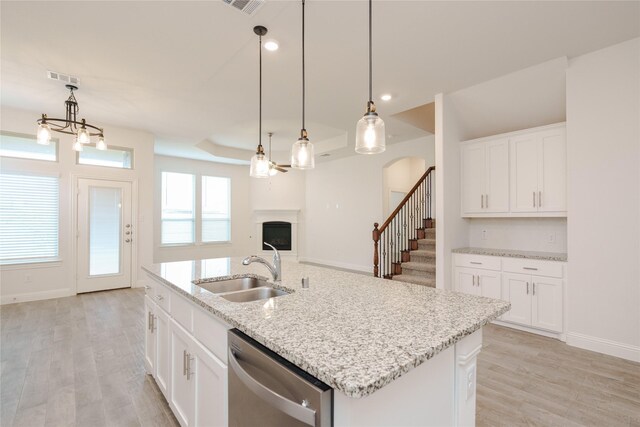 kitchen with a kitchen island with sink, pendant lighting, sink, stainless steel dishwasher, and white cabinets