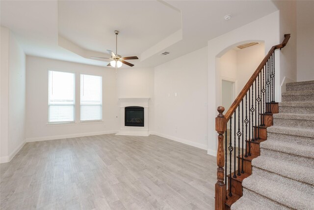 unfurnished living room featuring a raised ceiling, light hardwood / wood-style flooring, and ceiling fan