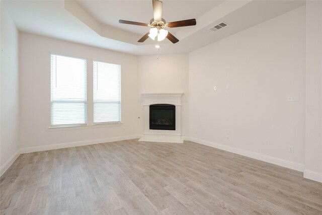 unfurnished living room with a tray ceiling, light hardwood / wood-style flooring, and ceiling fan