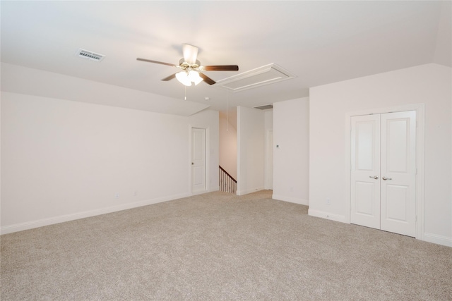 spare room featuring visible vents, baseboards, light colored carpet, attic access, and vaulted ceiling