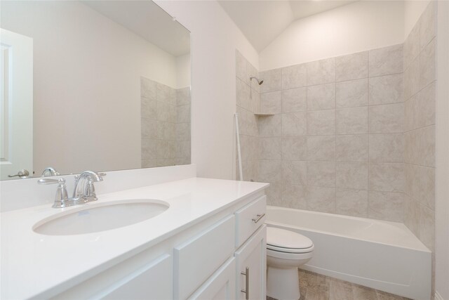 full bathroom featuring vaulted ceiling, toilet, tiled shower / bath, and vanity