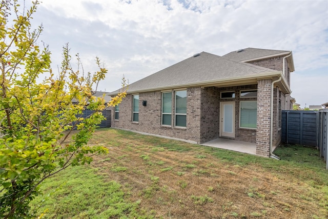 back of property featuring a fenced backyard, a yard, roof with shingles, brick siding, and a patio area