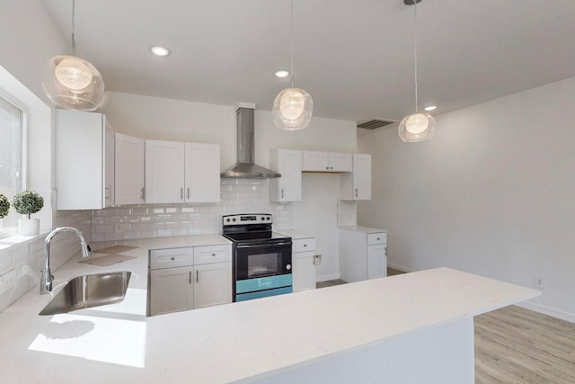 kitchen with stainless steel range with electric cooktop, wall chimney range hood, sink, white cabinets, and light hardwood / wood-style floors