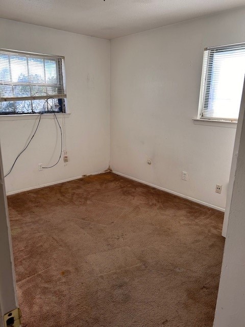 unfurnished room featuring a wealth of natural light and dark carpet