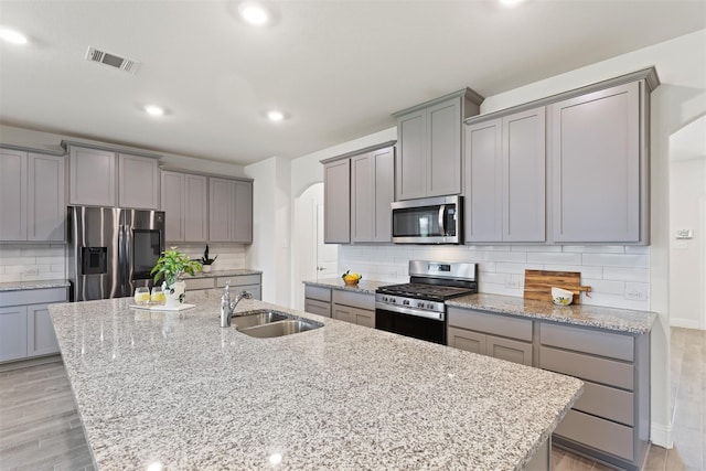 kitchen featuring light hardwood / wood-style flooring, stainless steel appliances, sink, an island with sink, and gray cabinetry