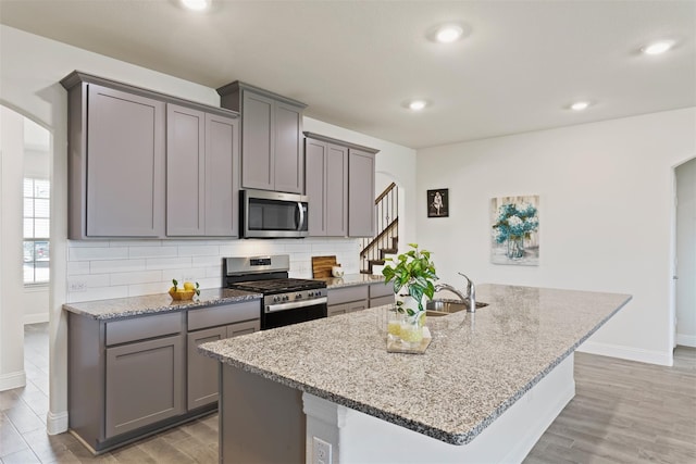 kitchen with light stone counters, appliances with stainless steel finishes, and a kitchen island with sink