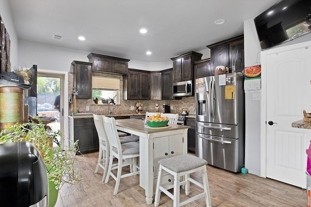 kitchen with dark brown cabinets, sink, decorative backsplash, appliances with stainless steel finishes, and light hardwood / wood-style floors