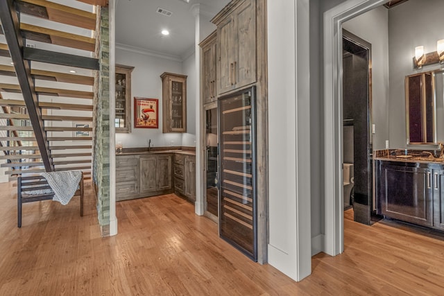 interior space featuring light wood-type flooring, crown molding, beverage cooler, and sink