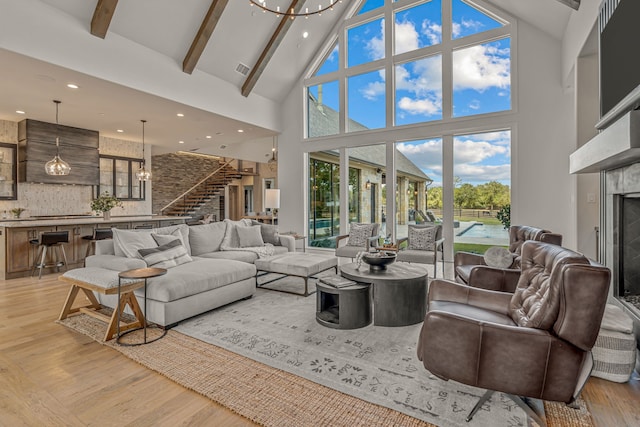 living room featuring light wood-type flooring, beamed ceiling, high vaulted ceiling, and a chandelier