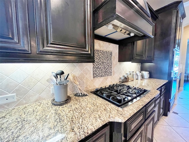 kitchen featuring backsplash, light tile patterned floors, custom range hood, light stone countertops, and appliances with stainless steel finishes