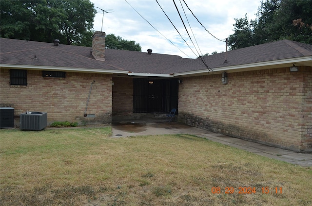 rear view of house with brick siding, a shingled roof, central AC, a chimney, and a yard