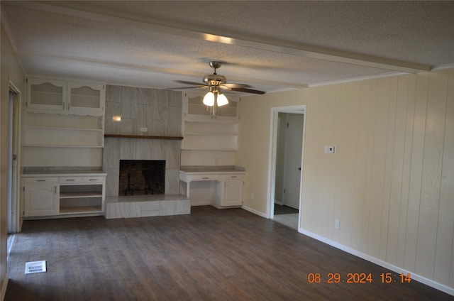 unfurnished living room featuring wooden walls, ceiling fan, dark wood-type flooring, a large fireplace, and a textured ceiling