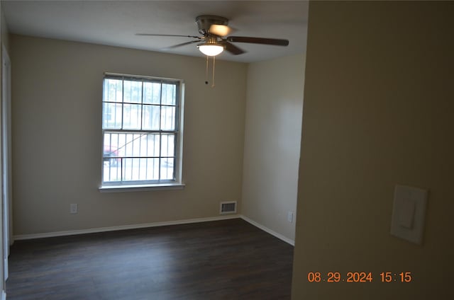 spare room featuring dark wood-type flooring, a ceiling fan, visible vents, and baseboards