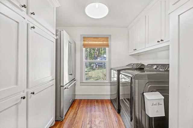 clothes washing area featuring separate washer and dryer, light hardwood / wood-style flooring, and cabinets