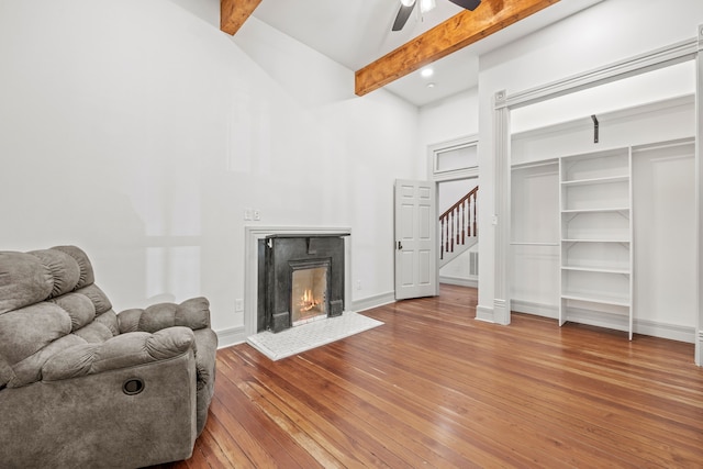 living room with ceiling fan, a premium fireplace, beam ceiling, and hardwood / wood-style floors