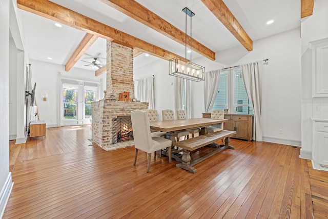 dining room featuring light wood-type flooring, beamed ceiling, ceiling fan, and a brick fireplace