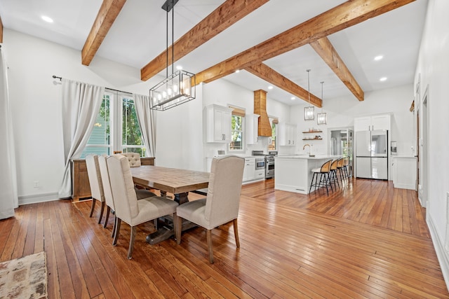 dining space with beamed ceiling, sink, and light hardwood / wood-style floors