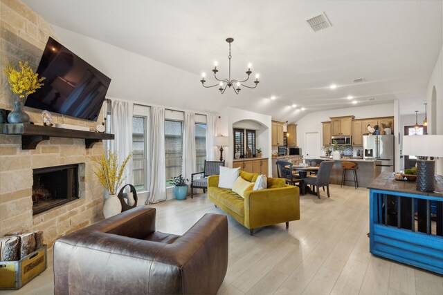 living room with vaulted ceiling, light hardwood / wood-style flooring, a notable chandelier, and a large fireplace