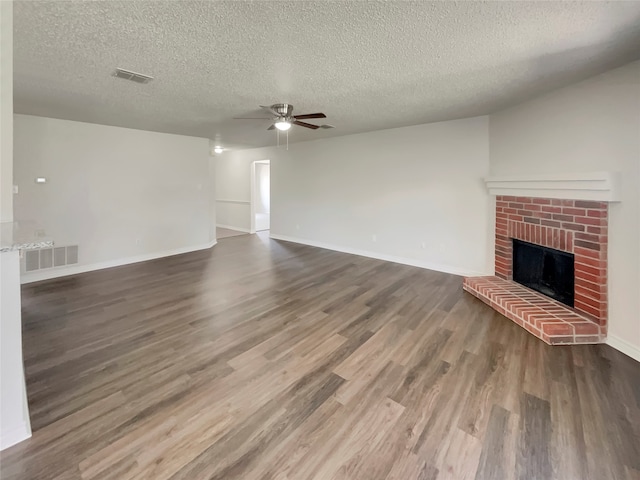 unfurnished living room featuring a textured ceiling, wood-type flooring, ceiling fan, and a brick fireplace