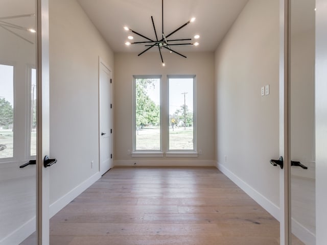 unfurnished room featuring an inviting chandelier and light wood-type flooring