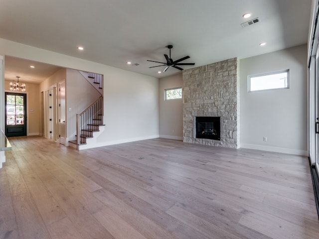 unfurnished living room with ceiling fan with notable chandelier, light hardwood / wood-style flooring, and a fireplace