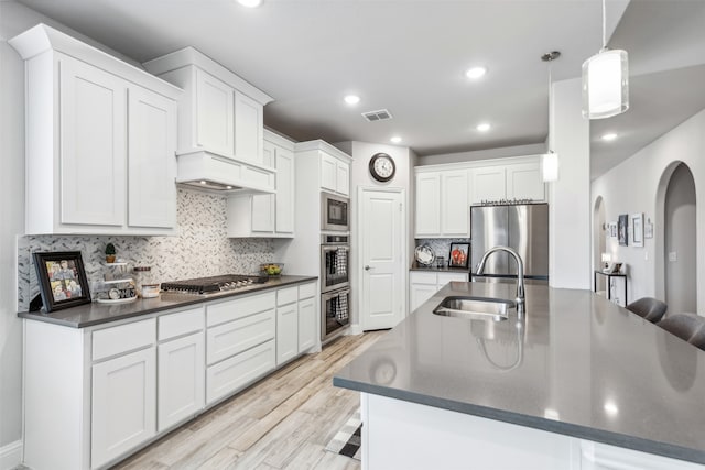 kitchen with light wood-type flooring, pendant lighting, sink, appliances with stainless steel finishes, and white cabinets