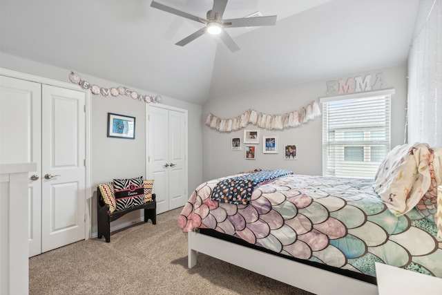 bedroom with ceiling fan, light colored carpet, vaulted ceiling, and multiple closets