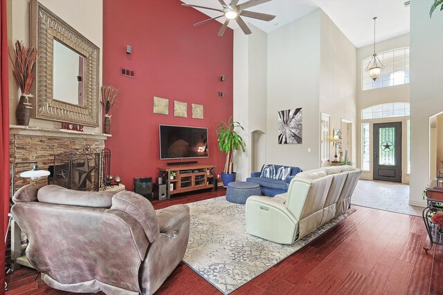 living room with wood-type flooring, a stone fireplace, high vaulted ceiling, and ceiling fan