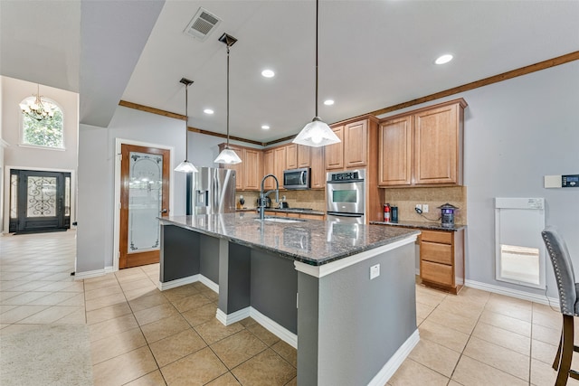 kitchen with a kitchen island with sink, dark stone countertops, pendant lighting, sink, and appliances with stainless steel finishes