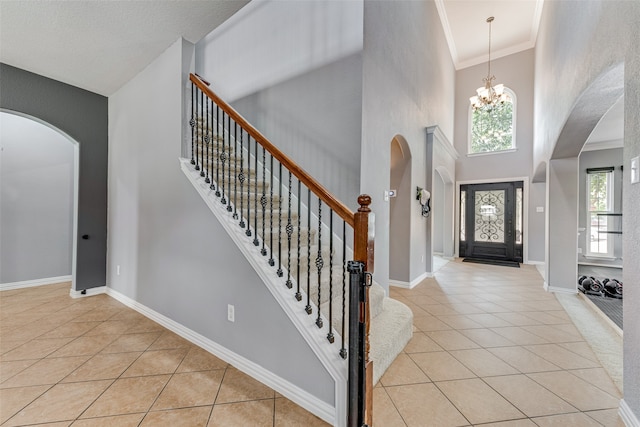 entryway with ornamental molding, a towering ceiling, light tile patterned floors, and a chandelier