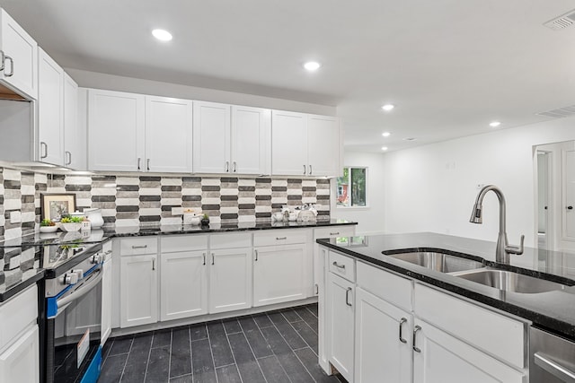 kitchen featuring stainless steel range with electric stovetop, white cabinetry, dark stone countertops, and sink