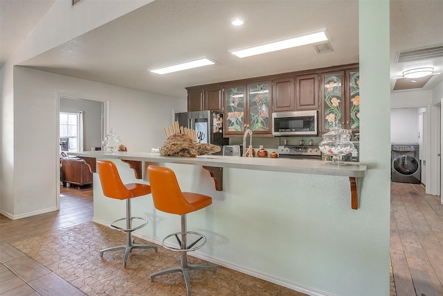 kitchen featuring kitchen peninsula, stainless steel appliances, washer / clothes dryer, and a breakfast bar area