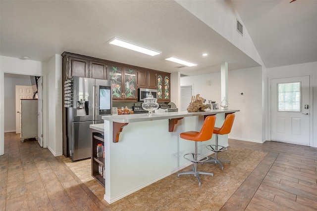 kitchen with light wood-type flooring, dark brown cabinetry, a breakfast bar area, and appliances with stainless steel finishes