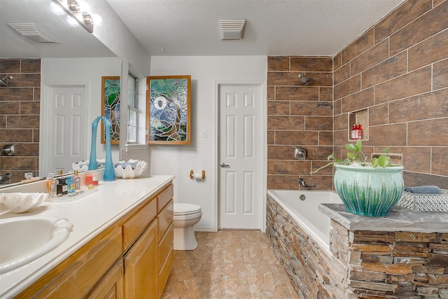 bathroom with vanity, a textured ceiling, tiled bath, and toilet