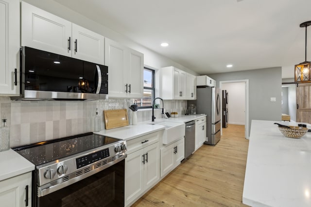 kitchen with white cabinetry, hanging light fixtures, stainless steel appliances, and light wood-type flooring