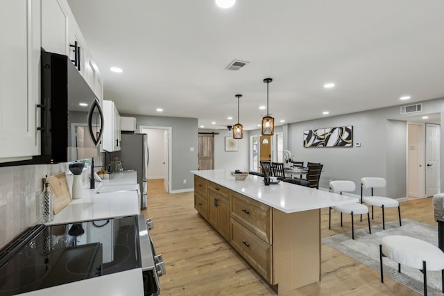 kitchen featuring light hardwood / wood-style flooring, appliances with stainless steel finishes, a spacious island, white cabinets, and decorative light fixtures