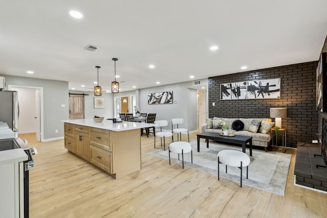 kitchen with light hardwood / wood-style flooring, hanging light fixtures, light brown cabinets, a kitchen island, and stainless steel appliances