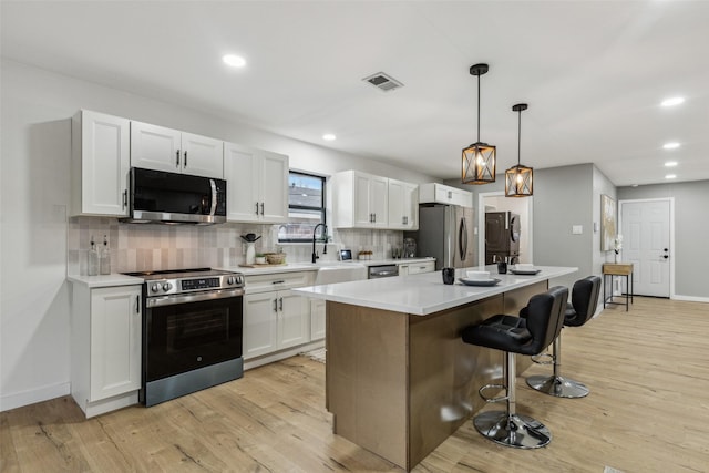 kitchen featuring white cabinetry, stainless steel appliances, a center island, light hardwood / wood-style floors, and a kitchen bar