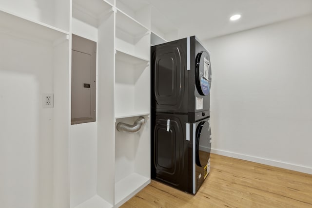 clothes washing area with stacked washer / dryer, electric panel, and wood-type flooring