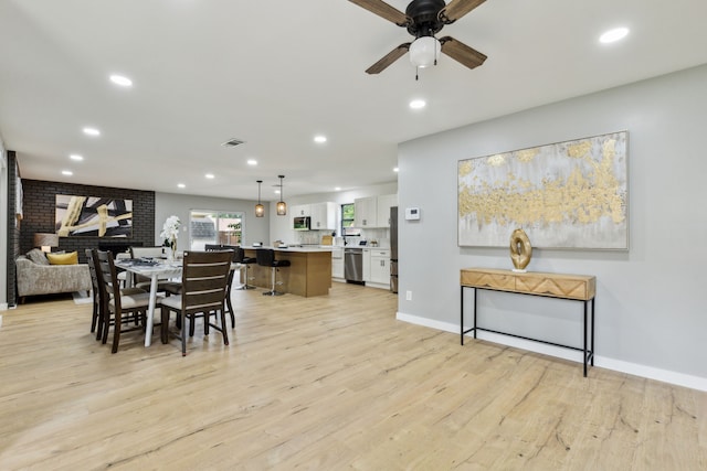 dining area featuring light hardwood / wood-style flooring, ceiling fan, and brick wall