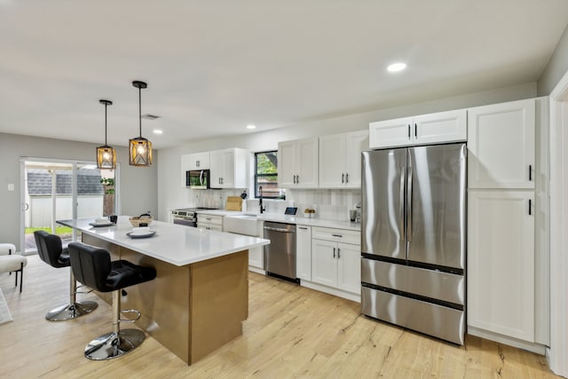 kitchen featuring decorative light fixtures, stainless steel appliances, white cabinets, and a kitchen island