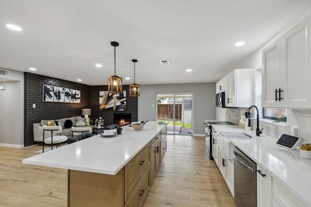 kitchen with pendant lighting, appliances with stainless steel finishes, a fireplace, white cabinets, and a kitchen island