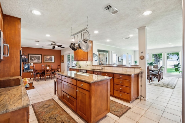 kitchen with ceiling fan, sink, a center island, and light stone countertops