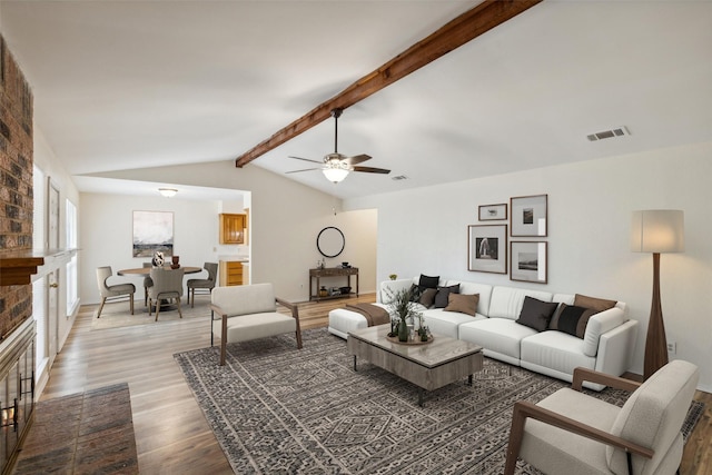 living room with a fireplace, light wood-type flooring, lofted ceiling with beams, and ceiling fan